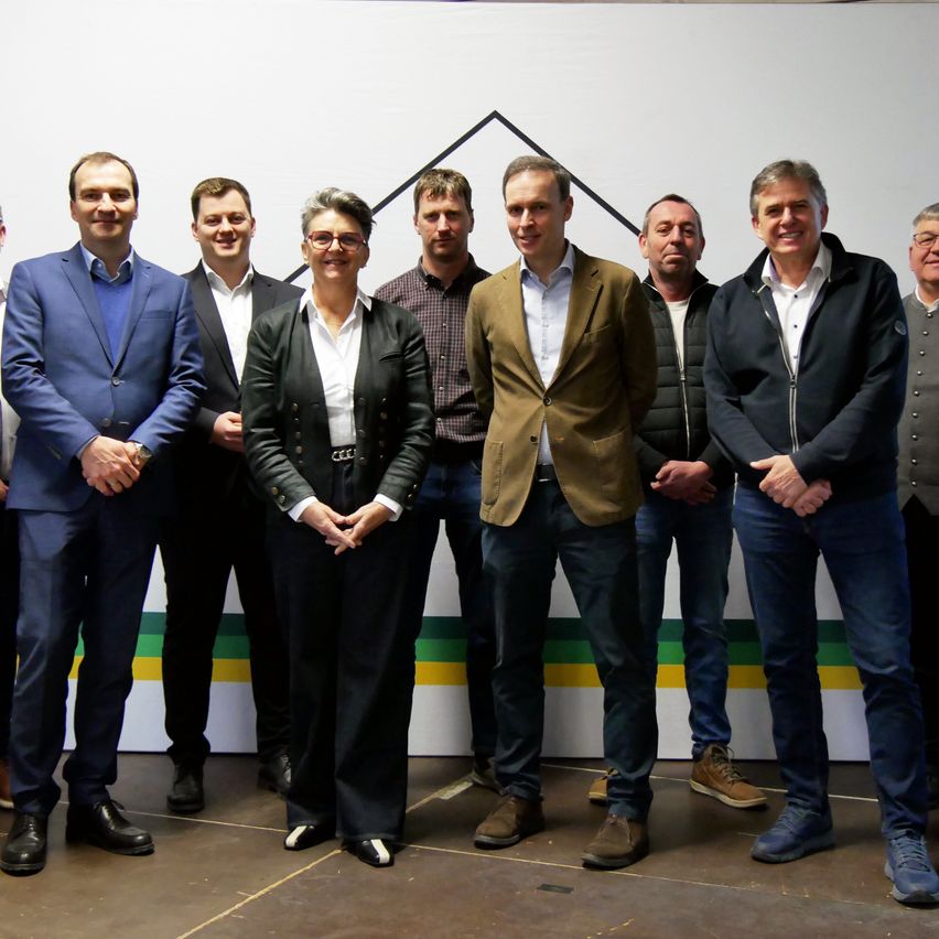 Eine Gruppe von Männern und Frauen in formeller Kleidung posiert für ein Foto vor einem Hintergrund mit einem dreieckigen Design.