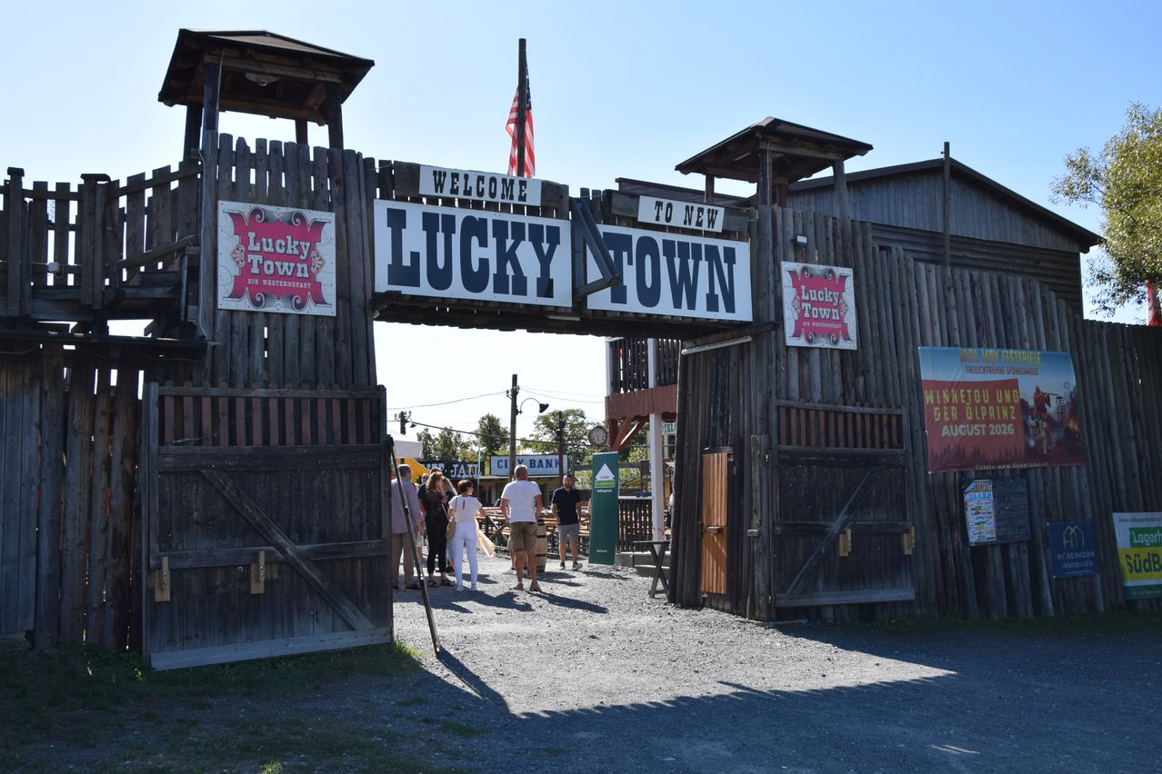 The entrance to Lucky Town, a themed area with wooden structures and signs. People are walking through the entrance.