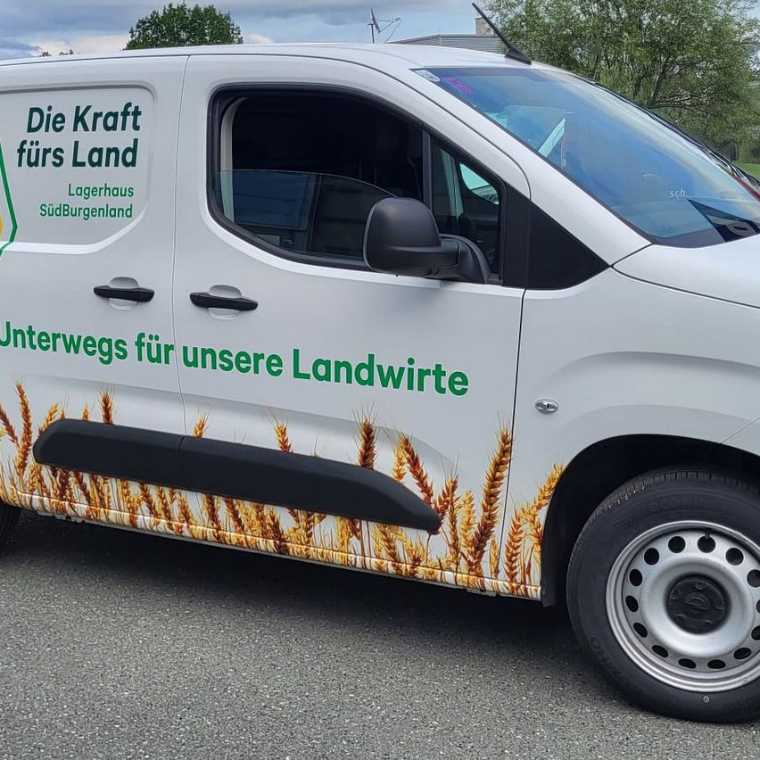 Ein weißer Lieferwagen mit dem Text Die Kraft fürs Land Lagerhaus Südburgenland Unterwegs für unsere Landwirte an der Seite. Der Lieferwagen hat Weizendesigns an der Seite.