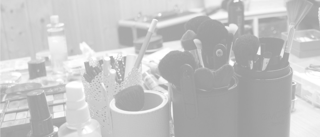 Der Arbeitsplatz einer Visagistin mit verschiedenen Pinseln, Make-up-Flaschen und einem Fenster. Die Pinseln befinden sich in Behältern und Make-up-Flaschen sind auf dem Schreibtisch verstreut.