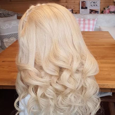 Eine Nahaufnahme des Rückens einer Person, die eine Kaskade von langen, welligen blonden Haaren auf einem Holztisch zeigt.