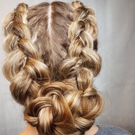 Eine Frau mit blondem Haar, gestylt in zwei großen Zöpfen, zu einem Dutt am Hinterkopf verdreht.