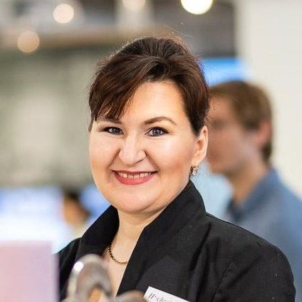 Eine lächelnde Frau steht bei einer Veranstaltung, trägt einen schwarzen Blazer und ein Namensschild mit der Aufschrift Hyggezimmerei. Vor ihr steht ein Pokal.