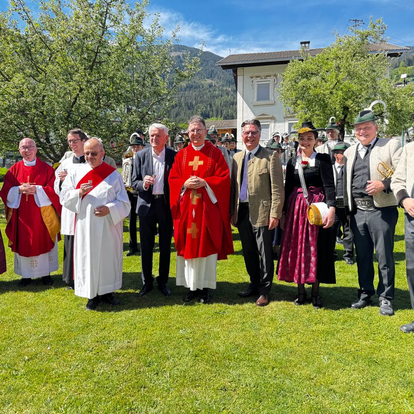 Eine Gruppe von Menschen in formeller Kleidung steht auf einem Rasen. Sie posieren für ein Foto mit einem Gebäude im Hintergrund.