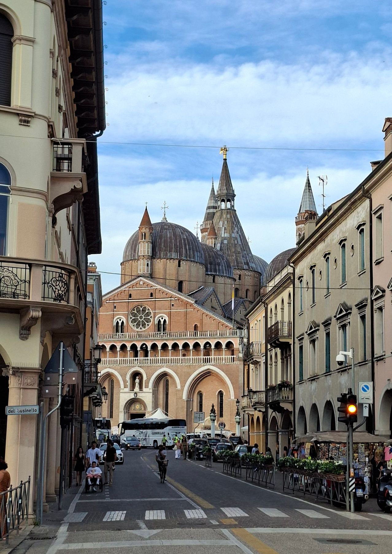 Eine Straße mit Gebäuden und Menschen. Eine Kathedrale mit Kuppeln und Türmen in der Ferne. Eine Straßenlaterne und eine Ampel.