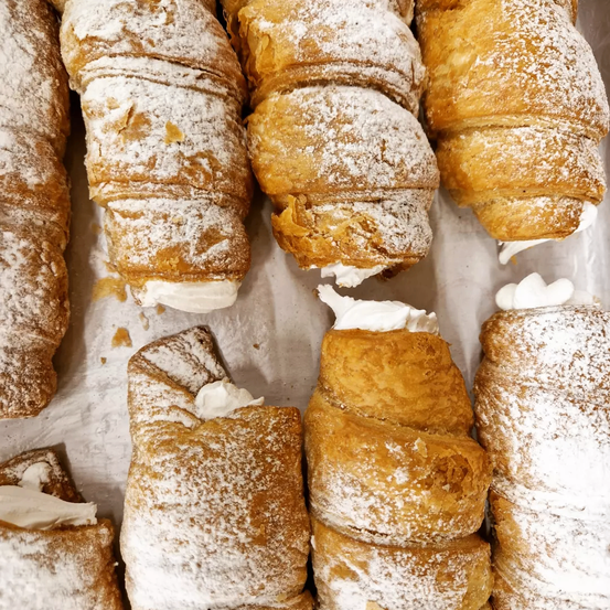 Eine Nahaufnahme von mehreren Croissants, die mit Puderzucker bestreut und mit etwas Sahne darauf sind. Sie sehen frisch aus und sind wahrscheinlich bereit, serviert zu werden.