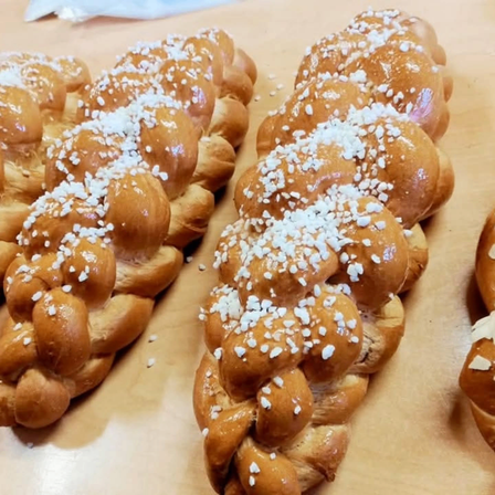 Zwei gebackene Challah-Brotlaibe liegen auf einer Holzoberfläche. Sie sind goldbraun mit einer Prise weißer Toppings.