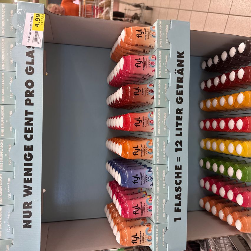 Eine Ausstellung von verschiedenen 12-Liter-Flaschen in einem Laden. Die Flaschen sind in verschiedenen Farben, und der Preis ist 4,99. Das Schild steht Nur Wenige Cent Pro Glas.