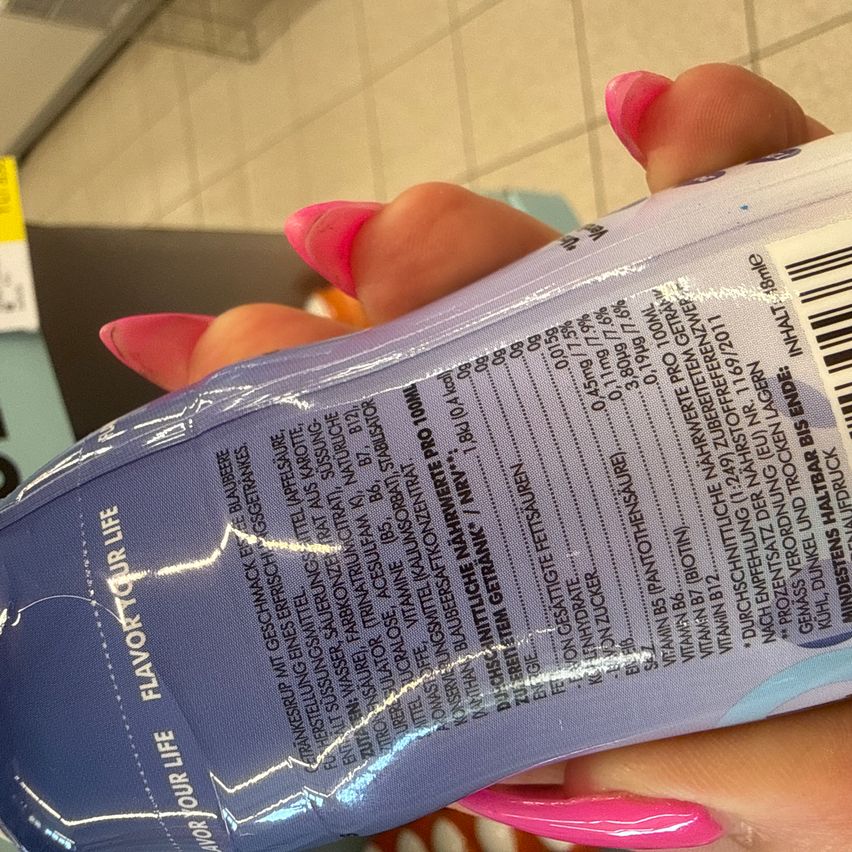 Eine Nahaufnahme einer Hand, die eine Flasche Sportgetränk mit Nährwertangaben und Zutaten auf dem Etikett hält.