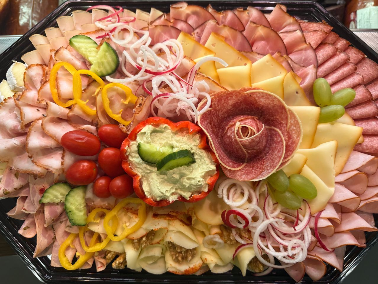 Eine große Charcuterie-Platte mit einer Auswahl an Fleisch, Käse, Gemüse und einer Dip-Mitte. Die Fleischsorten umfassen Schinken, Salami und Käse. Das Gemüse umfasst Tomaten, Gurken und Paprika. Die Dip-Mitte befindet sich in einer roten Paprika.