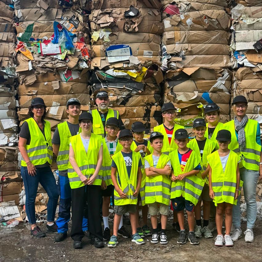 Eine Gruppe von Menschen in Warnwesten steht vor einem großen Haufen Pappkartons und anderen recycelbaren Materialien.