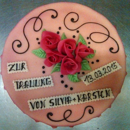 Ein rosa Kuchen mit Rosen und dem Text 'Zur Trallung von Silvia und Karsten' darauf. Der Kuchen hat einen weißen Rand und ist mit schwarzen Schwüngen und Punkten verziert. Das Datum '13.03.2015' ist ebenfalls auf dem Kuchen geschrieben.