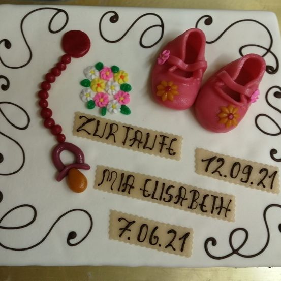 Ein Kuchen mit Babyschuhen und Blumen. Es trägt den Namen 'Mia Elisabeth' und die Daten '12.09.21' und '7.06.21' darauf geschrieben.