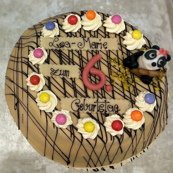 Ein Schokoladenkuchen mit einer Schokoladenspinne, buntem Zuckerguss und einem Panda, der einen Bambusstab hält. Es steht Lea-Marie, 6 und Geburtstag.