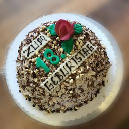 Ein Schokoladenkuchen mit einer roten Rose darauf. Der Kuchen hat die Aufschrift Zum 18. Geburtstag in weißer Glasur.