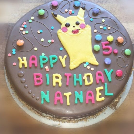Ein Schokoladenkuchen mit einem Pikachu-Charakter darauf. Der Kuchen hat eine Schokoladenglasur und bunte Streusel. Die Worte Happy Birthday Natanael sind in bunter Glasur geschrieben.
