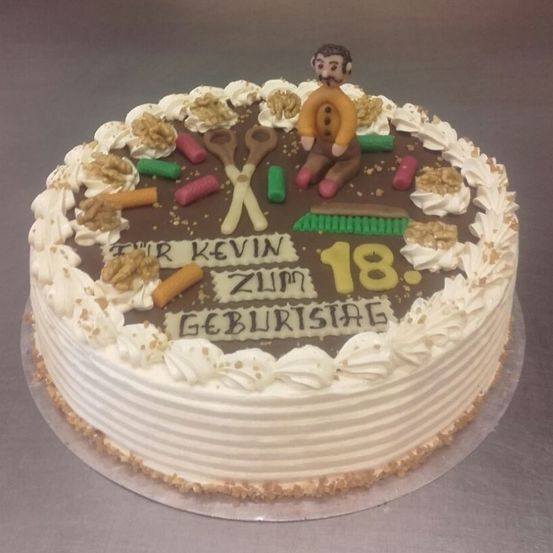 Ein Geburtstagskuchen mit einer Männerfigur, Scheren und einer Besen, auf dem 'Zum 18. Geburtstag Kevin' steht.