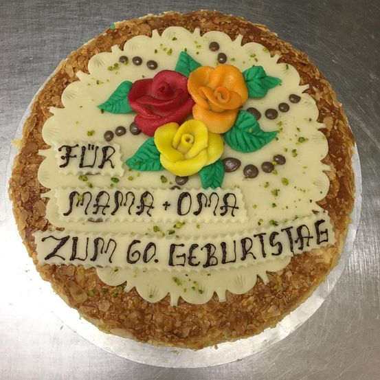 Ein Kuchen mit weißer Glasur und einer Nachricht für Mama und Oma, die ihren 60. Geburtstag feiern, mit roten, gelben und orangefarbenen Blumen.