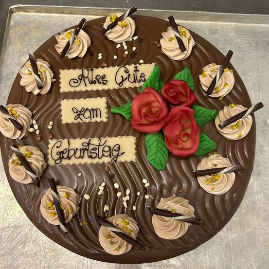 Ein Schokoladenkuchen, verziert mit Sahne, Schokoladenstückchen und roten Rosen, mit dem Text Alles Gute zum Geburtstag darauf geschrieben.