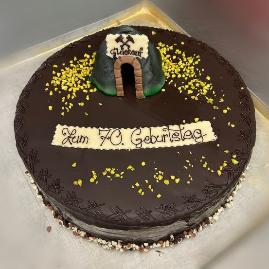 Ein Schokoladenkuchen mit einem grünen Tunnel und gelben Streuseln. Auf dem Kuchen steht 'Zum 70. Geburtstag'.