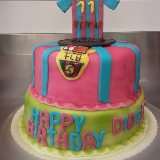 Ein mehrschichtiger Geburtstagskuchen mit der Aufschrift 'Happy Birthday Dion', auf dem ein Fußballtrikot platziert ist.