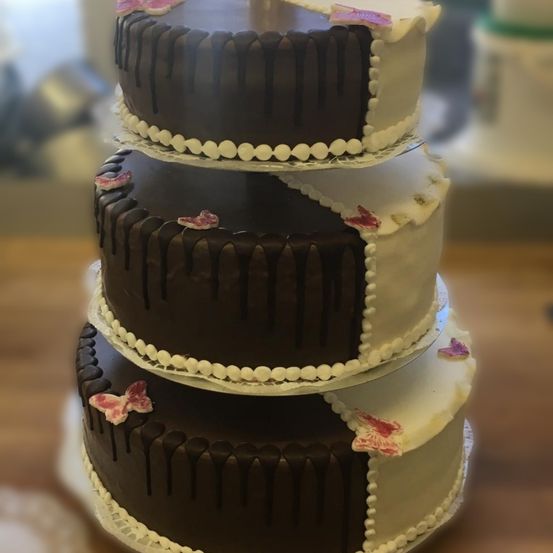 Ein vierstöckiger Schokoladenkuchen mit weißer Glasur und rosa Schmetterlingsdekorationen. Der Kuchen steht auf einer Holzoberfläche.