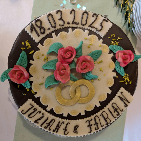 Ein Schokoladenkuchen mit den Namen Joanne und Fabian, verziert mit Rosen, Blättern und Hochzeitsringen, datiert vom 18. März 2023.