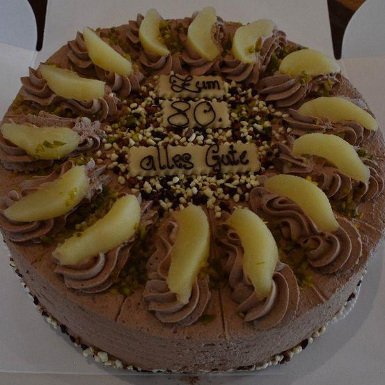 Ein Schokoladenkuchen mit einer weißen Cremeschicht und dekoriert mit Apfelscheiben und Nüssen. Der Kuchen hat eine weiße Nachricht obenauf geschrieben.