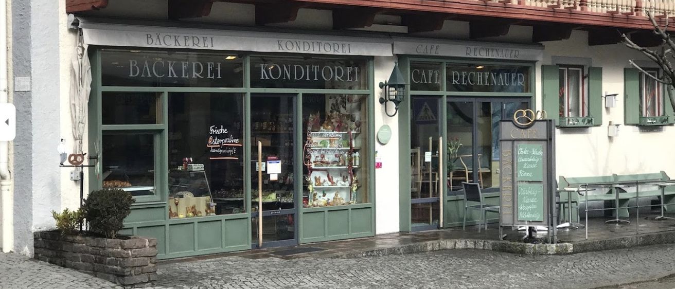 Eine Bäckerei und Cafe mit Balkon oben, ausgestellten Produkten und einem Schild.