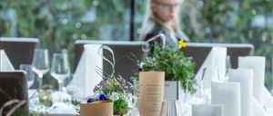 Ein verschwommenes Bild eines Restaurants mit einer Frau, die hinter einem Tisch sitzt, Blumen auf dem Tisch und Weingläsern.