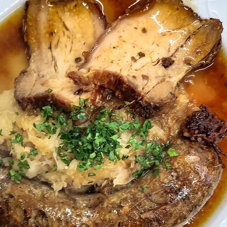 Ein Gericht mit Wurst und Fleisch mit Sauerkraut und Soße auf einem Teller. Die Wurst ist mit Petersilie garniert.