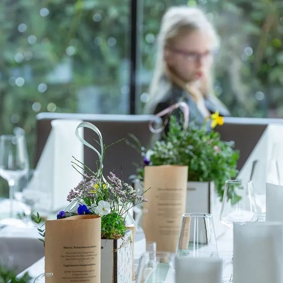 Ein Tisch für eine Mahlzeit mit Blumen, einer Speisekarte und einer verschwommenen Person im Hintergrund.