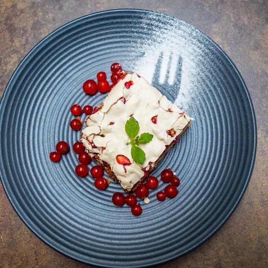 Ein Stück Dessert auf einem blauen Teller mit weißer Creme und roten Beeren. Ein Minzblatt ist obenauf.