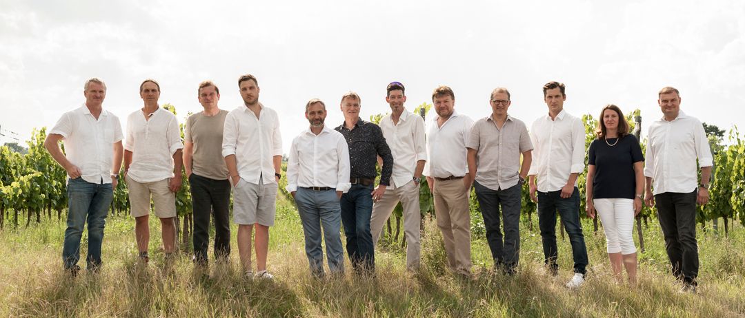 Elf Männer und eine Frau stehen auf einem Feld. Sie tragen alle weiße Hemden.