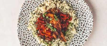 Ein Teller mit geometrischem Design hält ein Gericht aus Couscous mit roten Paprikaschoten und Fleisch, wahrscheinlich einem Hähnchenschenkel.