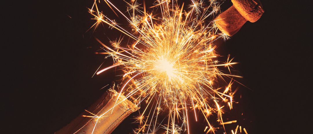 Eine Flasche Champagner mit Korken, der herausspringt, und Feuerwerk, das darum herum explodiert, in einer dunklen Umgebung.
