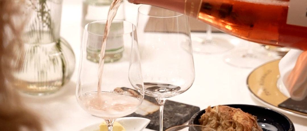 Eine Flasche Roséwein wird in ein Glas auf einem Tisch mit Brot, Butter und Blumen gegossen.