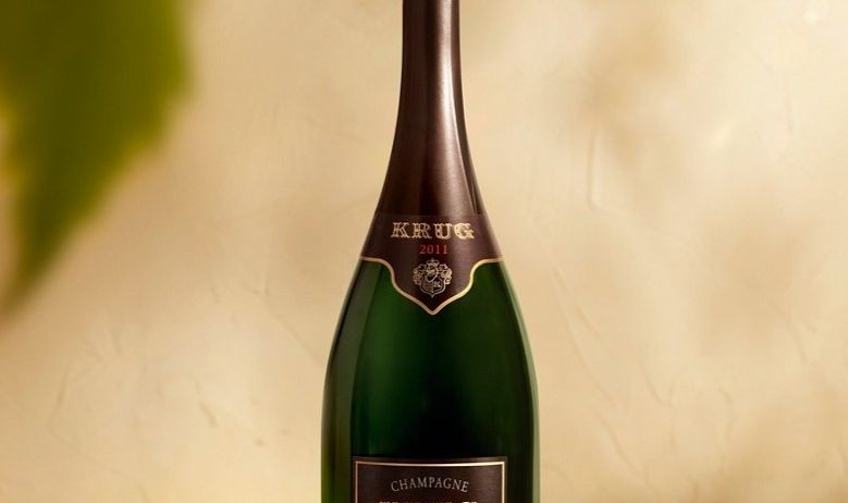 Eine Flasche Krug Champagner von 2011 wird auf einer weißen Oberfläche mit einem grünen Blatt im Hintergrund ausgestellt.