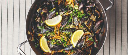 Eine Pfanne mit Muscheln, Zitrone und Kräutern auf einer gestreiften Oberfläche, begleitet von Brotscheiben.