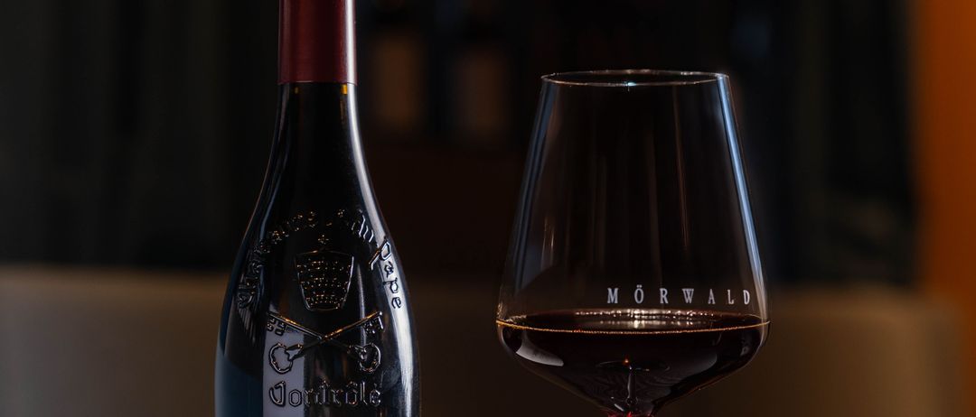 Eine Flasche Rotwein mit dem Etikett 'Telegramme' steht neben einem Glas Rotwein mit dem Wort 'Morwald' darauf.