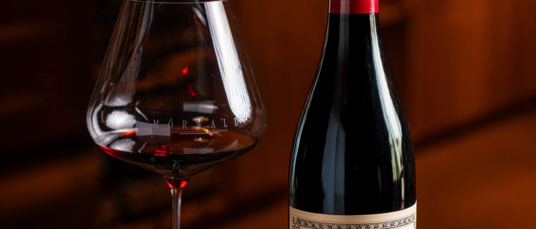 Eine Flasche Beaune Les Avaux Wein und ein Weinglas mit rotem Wein stehen auf einem Tisch.