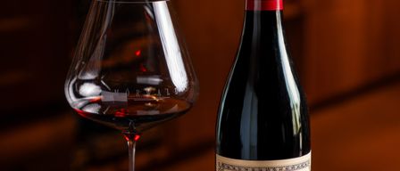 A bottle of Beaune Les Avaux wine and a wine glass with red wine are on a table.