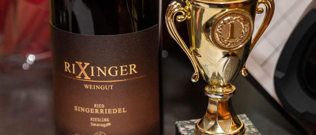 Eine Flasche Rixinger Wein steht neben einem goldenen Pokal auf einem Granitsockel mit der Aufschrift 'Morwald's Pub Quiz Champion'.