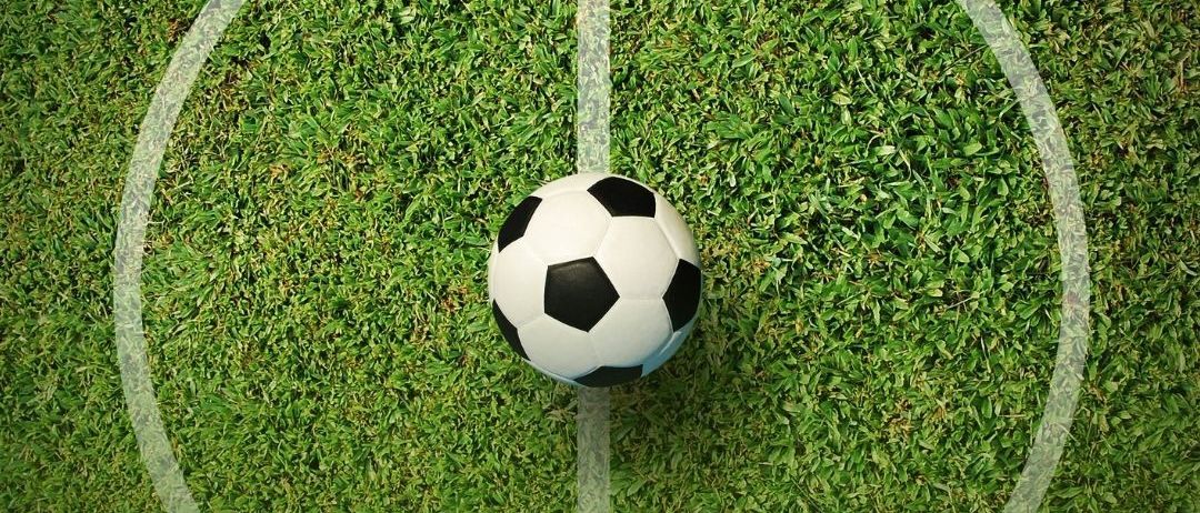 Ein Fußball liegt auf der Mitte eines Fußballfeldes, umgeben von weißen Linien.