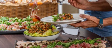 A group of people are serving themselves from a buffet table with various dishes, including salads, meats, and bread.