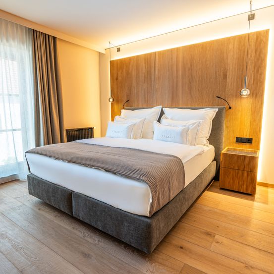 Ein geräumiges Schlafzimmer mit Holzböden und -wänden, einem großen Bett mit mehreren Kissen und einem Nachttisch mit Lampe.