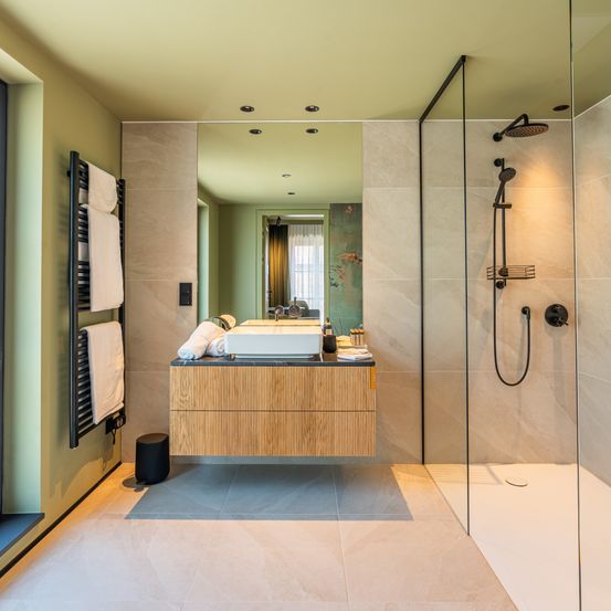 Ein Badezimmer mit beigefarbenen Fliesen, einem Holzschrank, einem weißen Waschbecken, einer Glasdusche und einem Handtuchhalter an der Wand.