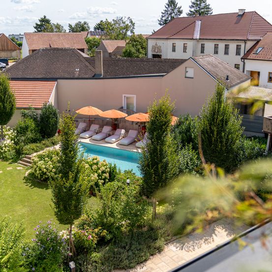 Luftaufnahme eines Resorts mit Swimmingpool, Liegestühlen und Sonnenschirmen. Das Resort hat einen modernen Architekturstil mit gefliesten Dächern und Glasfenstern.