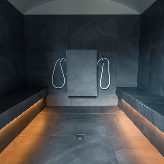 Ein leerer moderner Duschraum mit zwei Duschköpfen und zwei Bänken. Der Raum ist von einem warmen Licht erhellt, und der Boden hat ein einzigartiges Muster.