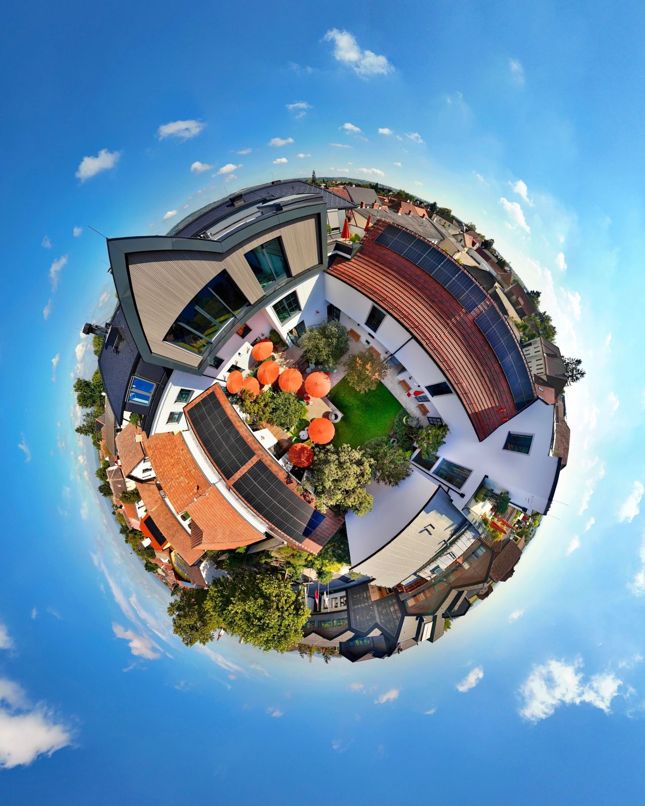 Eine sphärische Luftaufnahme eines modernen Architekturkomplexes, umgeben von Grünflächen, mit mehreren Gebäuden mit Solarpanelen und einem klaren blauen Himmel.